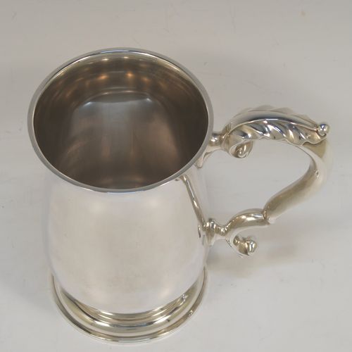 A very handsome Sterling Silver pint tankard or mug, having a plain round bellied body, a scroll handle with anthemion leaf thumb-piece, and sitting on a pedestal foot. This elegant sterling silver pint mug was made by Goldsmiths and Silversmiths of London in 1938. The dimensions of this fine hand-made silver pint tankard are height 14 cms (5.5 inches), diameter at top 8.5 cms (3.3 inches), and it weighs approx. 295g (9.5 troy ounces). Please note that the inside is finished off in a Butler finish which is not as bright as the outside.   