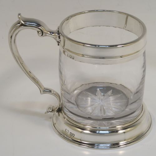 A handsome and unusual Antique Sterling Silver and glass pint tankard or mug, having a plain round hand-blown glass body with a star-cut base, together with silver mounts and a side scroll handle. This elegant silver and glass pint mug was made Carrington and Co., of London in 1915. The dimensions of this fine hand-made antique silver and glass pint mug or tankard are height 11.5 cms (4.5 inches), and diameter at top 8 cms (3 inches),   