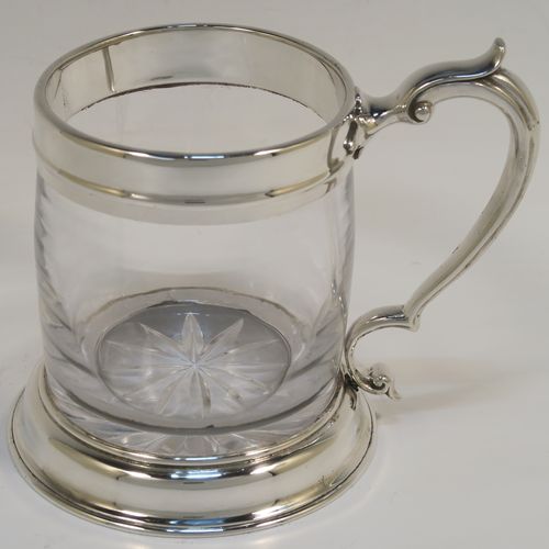 A handsome and unusual Antique Sterling Silver and glass pint tankard or mug, having a plain round hand-blown glass body with a star-cut base, together with silver mounts and a side scroll handle. This elegant silver and glass pint mug was made Carrington and Co., of London in 1915. The dimensions of this fine hand-made antique silver and glass pint mug or tankard are height 11.5 cms (4.5 inches), and diameter at top 8 cms (3 inches),   