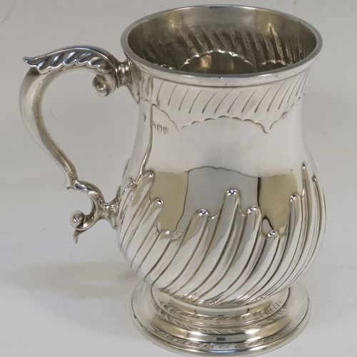 A handsome Antique Victorian Sterling Silver pint tankard or mug, having a round bellied body with hand-chased swirl-fluted decoration, a scroll side handle with an anthemion leaf thumb-piece, and sitting on a pedestal foot. This beautiful silver mug was made by Charles Stuart Harris of London in 1892. The dimensions of this fine hand-made antique silver pint mug or tankard are height 14 cms (5.5 inches), diameter at top 9 cms (3.5 inches), and it weighs approx. 372g (12 troy ounces).   