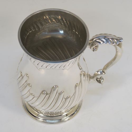 A handsome Antique Victorian Sterling Silver pint tankard or mug, having a round bellied body with hand-chased swirl-fluted decoration, a scroll side handle with an anthemion leaf thumb-piece, and sitting on a pedestal foot. This beautiful silver mug was made by Charles Stuart Harris of London in 1892. The dimensions of this fine hand-made antique silver pint mug or tankard are height 14 cms (5.5 inches), diameter at top 9 cms (3.5 inches), and it weighs approx. 372g (12 troy ounces).   