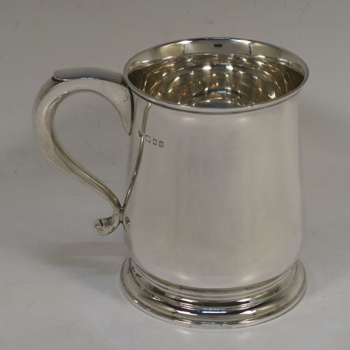 A heavy and very handsome Sterling Silver pint tankard or mug, having a plain round body with straight sides and a tucked under belly, a scroll side-handle, and sitting on a pedestal foot. This elegant silver pint mug was made by Goldsmiths and Silversmiths of London in 1928. The dimensions of this fine hand-made silver pint mug or tankard are height 11.5 cms (4.5 inches), diameter at top 8.5 cms (3.3 inches), and it weighs approx. 368g (11.9 troy ounces).   