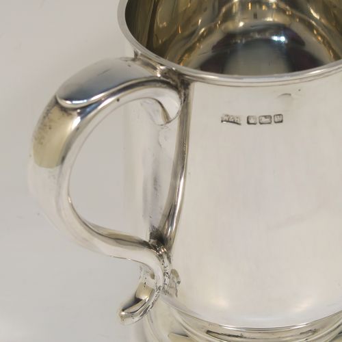 A handsome antique Sterling Silver pint tankard or mug, having a plain round body with straight sides and a tucked under belly, a scroll side-handle, and sitting on a pedestal foot. This elegant silver pint mug was made by Walker and Hall of Sheffield in 1917. The dimensions of this fine hand-made antique silver pint mug or tankard are height 13 cms (5 inches), diameter at top 8.5 cms (3.3 inches), and it weighs approx. 297g (9.6 troy ounces).  