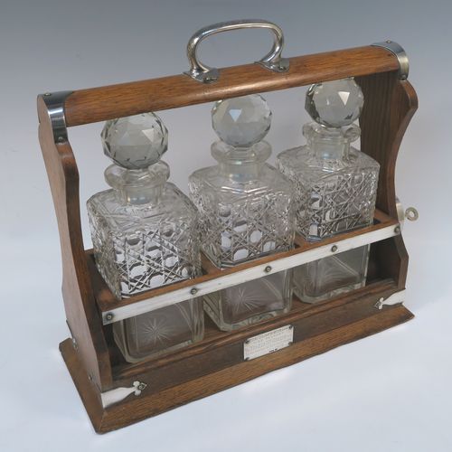 A very handsome Antique Silver-plated and wood framed three-bottle tantalus, with original hand-cut crystal decanters and stoppers, all in an oak (poss.) wooden frame with silver-plated and nickel pinned mounts, with a patented lock mechanism and key. The presentation inscription is engraved onto a sterling silver plaque with hallmarks, which indicate that this beautiful antique silver-plated and wood tantalus was made by Walker and Hall of Birmingham in 1912. The dimensions of this fine hand-made antique three-bottle tantalus are length 36 cms (14 inches), height 32 cms (12.5 inches), and depth 14 cms (5.5 inches).   