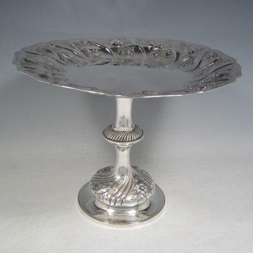 Antique Victorian sterling silver tazza dish, having a round body with hand-chased floral and fruit decoration, sitting on a pedestal foot with matching decoration and swirl fluting. Made by Henry Holland of London in 1874. The dimensions of this fine hand-made silver tazza dish are height 21 cms (8.25 inches), diameter 26 cms (10.25 inches), and it weighs approx. 838g (27 troy ounces).