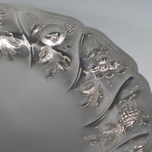 Antique Victorian sterling silver tazza dish, having a round body with hand-chased floral and fruit decoration, sitting on a pedestal foot with matching decoration and swirl fluting. Made by Henry Holland of London in 1874. The dimensions of this fine hand-made silver tazza dish are height 21 cms (8.25 inches), diameter 26 cms (10.25 inches), and it weighs approx. 838g (27 troy ounces).