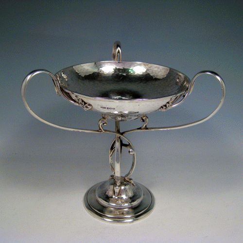    Sterling silver Arts & Crafts style hand-hammered tazza dish with three scroll handles, sitting on a pedestal foot above which the handles are inter-twined. Made by James Dixon of Sheffield in 1912. Height 21 cms (8.25 inches), diameter of bowl 16.5 cms (6.5 inches). Weight approx. 20.5 troy ounces (636g).