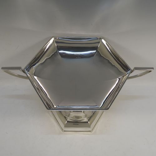 A very handsome Sterling Silver tazza dish or bowl, having a plain hexagonal paneled body, with two cast side-handles having scroll-leaf terminals, and sitting on a matching pedestal foot. This beautiful tazza dish was made by Walker and Hall of Sheffield in 1927. The dimensions of this fine hand-made silver tazza bowl or dish are height 16 cms (6.3 inches), width across handles 31 cms (12.25 inches), and it weighs approx. 638g (20.6 troy ounces).   