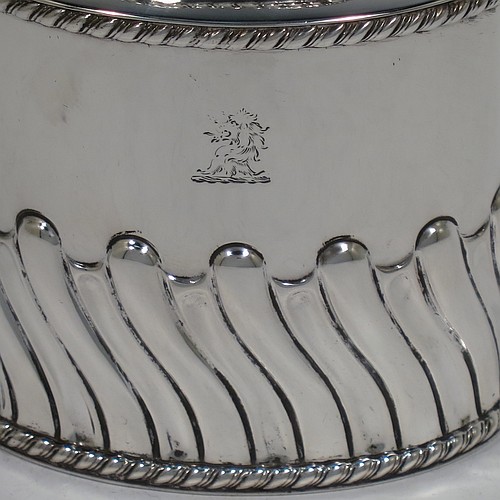 A very handsome Antique Victorian sterling silver tea caddy box, having an oval straight-sided body with hand-chased swirl-fluted decoration, applied gadroon borders, and a pull-off lid which was used as a measure, all sitting on a flat base. Made by Henry Atkins of Sheffield in 1895. The dimensions of this fine antique silver tea caddy box are height 9 cms (3.5 inches), length 8 cms (3 inches), width 5.5 cms (2.25 inches), and it weighs approx. 146g (4.7 troy ounces). Please note that this item has a part-crest on the main body.