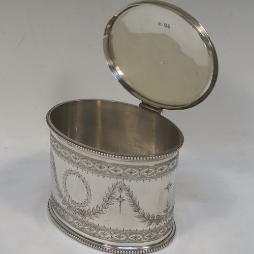 A very pretty Antique Victorian Sterling Silver tea caddy box, having an oval straight-sided body with applied bead borders, a cast urn-shaped finial sitting on a flat hinged lid, with hand-engraved bands top and bottom, together with neoclassical style engraved swags surrounding round vacant cartouches on either side, and all sitting on a flat base. This beautiful antique silver tea caddy box was made by Henry Wilkinson and Co., of London in 1875. The dimensions of this fine hand-made antique silver tea caddy box are height 11 cms (4.3 inches), length 13 cms (5 inches), depth 10 cms (4 inches), and it weighs approx. 407g (13 troy ounces).  