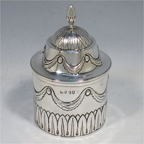 An Antique Georgian Sterling Silver tea caddy box, having a round straight-sided body with hand-chased Neoclassical style swags and anthemion leaves, with applied reeded borders, a pull-off domed lid with cast acorn finial, and all sitting on a flat base. Made by the Lias Brothers of London in 1826. The dimensions of this fine antique silver tea caddy box are height 12 cms (4.75 inches), diameter 7 cms (2.75 inches), and it weighs approx. 190g (6 troy ounces).    