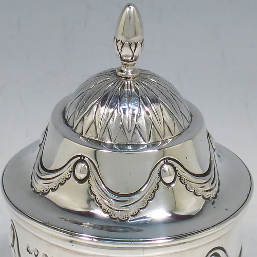 An Antique Georgian Sterling Silver tea caddy box, having a round straight-sided body with hand-chased Neoclassical style swags and anthemion leaves, with applied reeded borders, a pull-off domed lid with cast acorn finial, and all sitting on a flat base. Made by the Lias Brothers of London in 1826. The dimensions of this fine antique silver tea caddy box are height 12 cms (4.75 inches), diameter 7 cms (2.75 inches), and it weighs approx. 190g (6 troy ounces).    