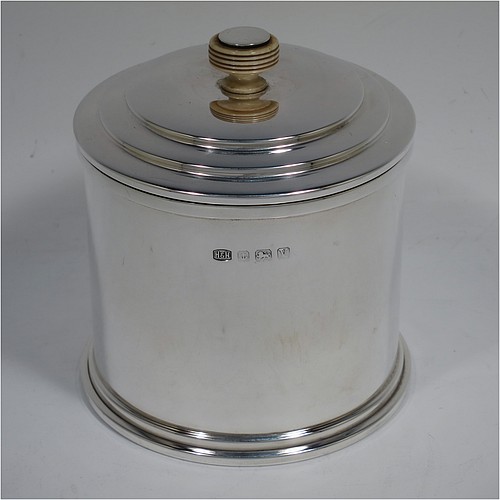 A very handsome Art Deco style Sterling silver tea caddy box, having a plain cylindrical body with straight sides and applied reeded borders, a lift-off lid with stepped decoration and a bone finial, and sitting on a collet foot. Made by Hukin and Heath of Birmingham in 1945. The dimensions of this fine hand-made Art Deco silver tea caddy box are height 10 cms (4 inches), diameter 9 cms (3.5 inches), and it weighs approx. 246g (7.9 troy ounces).    