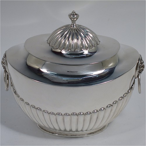 An Antique Edwardian Sterling Silver tea caddy box, having an oval bellied body with hand-chased half-fluted decoration, two lion-mask and ring side-handles, a hinged domed lid with matching fluting and a cast urn finial, and all sitting on a collet foot. Made by Goldsmiths and Silversmiths of London in 1906. The dimensions of this fine hand-made antique silver tea caddy box are height 11 cms (4.25 inches), length 12.5 cms (5 inches), width 8 cms (3.25 inches), and it weighs approx. 198g (6.4 troy ounces).   