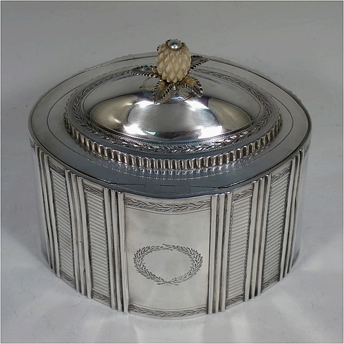 A very handsome Antique Georgian Sterling Silver tea caddy box, having an oval straight-sided body with hand-engraved panels between hand-chased vertical bands of fluting, with hand-engraved laurel-leaf cartouches on either side, a fluted and domed lid with flat invisible hinge and pineapple finial, all sitting on a flat base and with its original lock and key. Made by Henry Chawner of London in 1795. The dimensions of this fine hand-made antique silver tea caddy box are height 16 cms (6.25 inches), length 14 cms (5.5 inches), width 9.5 cms (3.75 inches), and it weighs approx. 333g (10.7 troy ounces).   