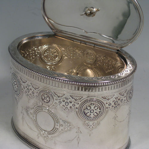    Antique Victorian sterling silver tea caddy box, having an oval straight-sided body, cast oval finial sitting on a lid with flat hidden hinge, applied bead edges top and bottom, with hand-chased and engraved floral work, and two vacant cartouches either side. Made by the Barnard Brothers of London in 1872. Height 13 cms (5 inches), length 14 cms (5.55 inches), width 10 cms (4 inches). Weight approx. 405g (13.1 troy ounces).