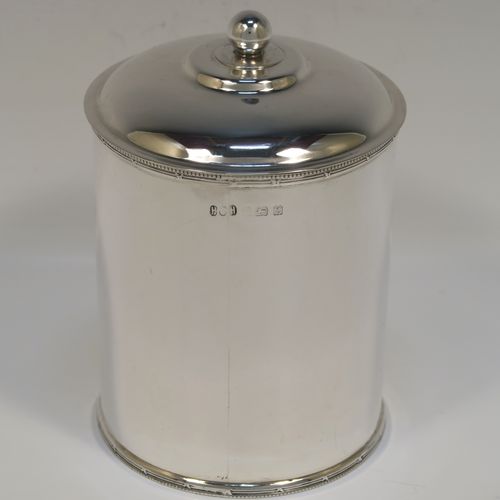 A very handsome Antique Sterling Silver tea caddy box, having a plain cylindrical body with straight sides and applied bead, ribbon and reed top and bottom borders, a slightly domed lift-off lid with a ball finial, and sitting on a flat base. This elegant silver tea caddy box was made by Hukin and Heath of Birmingham in 1924. The dimensions of this fine hand-made antique silver tea caddy box are height 13 cms ( 5inches), diameter 9 cms (3.5 inches), and it weighs approx. 255g (8.2 troy ounces).   