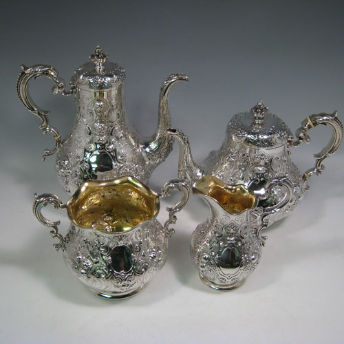 Antique Victorian sterling silver four-piece tea and coffee service, having round hand-chased bodies with floral decoration, hinged lids and finials, insulated handles, and gold-gilt interiors. Made by Robert Hennell of London in 1858/59. Height of coffee pot 25.5 cms (10 inches), length of teapot 25.5 cms (10 inches). Total weight approx. 2,340g (75.5 troy ounces).