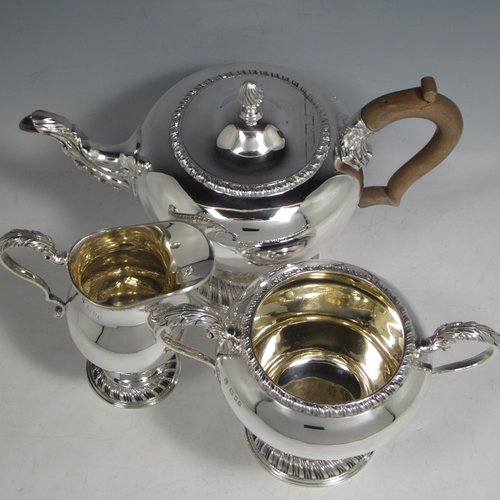 Sterling silver heavy three-piece tea set, consisting of teapot, sugar bowl, and cream jug, in a round baluster style having plain bodies, with applied gadroon borders, cast scroll handles and gold-gilt interiors, the teapot with a hinged lid and flame finial, a wooden insulated handle, and all sitting on pedestal feet with hand-chased swirl fluting. Made by Charles Townley and John Thomas, of London in 1913. The dimensions of this fine hand-made silver tea set are height of teapot 18 cms (7 inches), length 26.5 cms (10.5 inches), and it weighs a total of approx. 1,490g (48 troy ounces).    