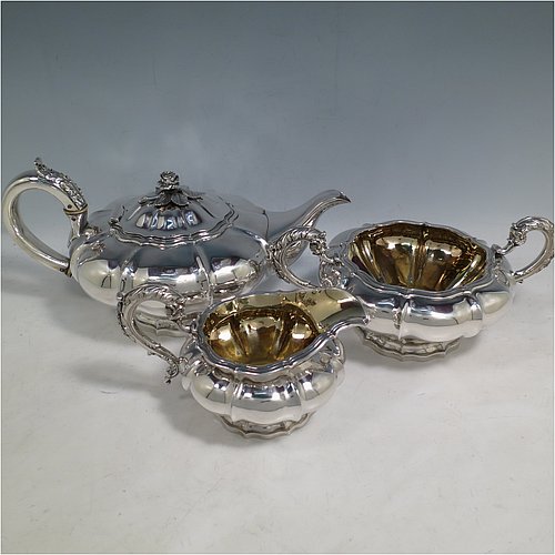 An Antique Georgian Sterling Silver three-piece tea set, having a teapot, sugar bowl and cream jug. The bodies all hand-chased with Melon style fluted decoration, the sugar and creamer with gold-gilt interiors and cast anthemion leaf handles, the teapot with silver insulated handle and cast rose finial, and all sitting on pedestal feet. Made by Rebecca Emes and John Barnard of London in 1826. The dimensions of this fine hand-made antique silver tea service are length of teapot 29 cms (11.5 inches), height 14 cms (5.5 inches), and it weighs a total of approx. 1,362g (44 troy ounces).    