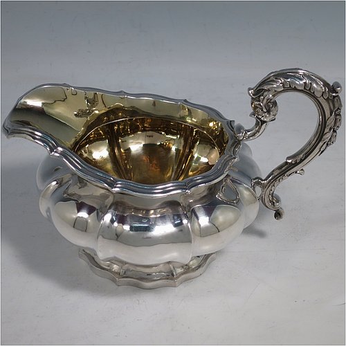 An Antique Georgian Sterling Silver three-piece tea set, having a teapot, sugar bowl and cream jug. The bodies all hand-chased with Melon style fluted decoration, the sugar and creamer with gold-gilt interiors and cast anthemion leaf handles, the teapot with silver insulated handle and cast rose finial, and all sitting on pedestal feet. Made by Rebecca Emes and John Barnard of London in 1826. The dimensions of this fine hand-made antique silver tea service are length of teapot 29 cms (11.5 inches), height 14 cms (5.5 inches), and it weighs a total of approx. 1,362g (44 troy ounces).    