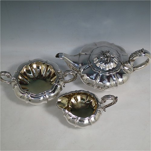 An Antique Georgian Sterling Silver three-piece tea set, having a teapot, sugar bowl and cream jug. The bodies all hand-chased with Melon style fluted decoration, the sugar and creamer with gold-gilt interiors and cast anthemion leaf handles, the teapot with silver insulated handle and cast rose finial, and all sitting on pedestal feet. Made by Rebecca Emes and John Barnard of London in 1826. The dimensions of this fine hand-made antique silver tea service are length of teapot 29 cms (11.5 inches), height 14 cms (5.5 inches), and it weighs a total of approx. 1,362g (44 troy ounces).    