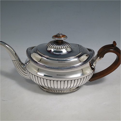 An Antique Georgian Sterling Silver three-piece early Regency style tea set, having a teapot, sugar bowl and cream jug. The oval bodies all hand-chased with half-fluted decoration, the sugar and creamer with gold-gilt interiors, the teapot with wooden handle and finial, and an invisibly hinged lid, all with applied gadroon borders, and all sitting on pedestal feet. Made by Daniel Pontifex London in 1805. The dimensions of this fine hand-made antique silver tea service are length of teapot 30 cms (11.75 inches), height 15 cms (6 inches), and it weighs a total of approx. 1,170g (38 troy ounces).    