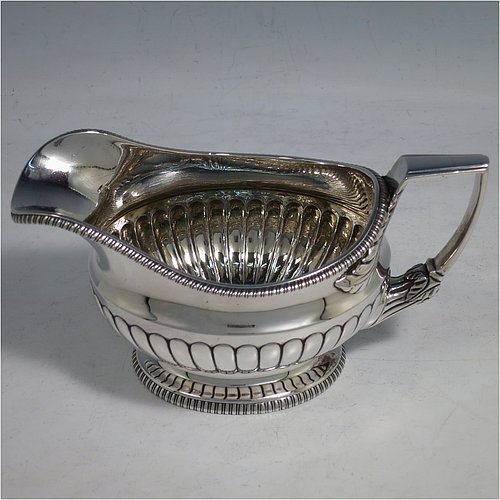 An Antique Georgian Sterling Silver three-piece early Regency style tea set, having a teapot, sugar bowl and cream jug. The oval bodies all hand-chased with half-fluted decoration, the sugar and creamer with gold-gilt interiors, the teapot with wooden handle and finial, and an invisibly hinged lid, all with applied gadroon borders, and all sitting on pedestal feet. Made by Daniel Pontifex London in 1805. The dimensions of this fine hand-made antique silver tea service are length of teapot 30 cms (11.75 inches), height 15 cms (6 inches), and it weighs a total of approx. 1,170g (38 troy ounces).    