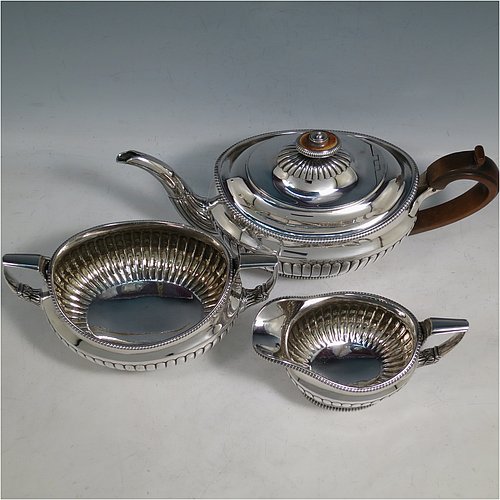 An Antique Georgian Sterling Silver three-piece early Regency style tea set, having a teapot, sugar bowl and cream jug. The oval bodies all hand-chased with half-fluted decoration, the sugar and creamer with gold-gilt interiors, the teapot with wooden handle and finial, and an invisibly hinged lid, all with applied gadroon borders, and all sitting on pedestal feet. Made by Daniel Pontifex London in 1805. The dimensions of this fine hand-made antique silver tea service are length of teapot 30 cms (11.75 inches), height 15 cms (6 inches), and it weighs a total of approx. 1,170g (38 troy ounces).    