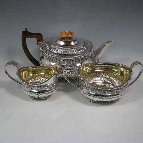 Antique Georgian sterling silver three-piece Regency style tea set, having a teapot, sugar bowl and cream jug. The bodies all hand-chased with roses and converging flute decoration, with applied gadroon borders, the sugar and creamer with gold-gilt interiors, the teapot with wooden handle and ivory finial, and an invisibly hinged lid, and all sitting on four cast foliate feet. Made by Charles Fox I of London in 1821. The dimensions of this fine hand-made silver tea service are length of teapot 29 cms (11.5 inches), height 17 cms (6.75 inches), and it weighs a total of approx. 1,260g (41 troy ounces). 