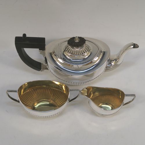 A pretty Antique Sterling Silver Bachelor three-piece tea set, having oval shaped bodies, with half-fluted hand-chased decoration, gold-gilt interiors and reeded handles on the sugar & cream jug, a wooden handle and finial on the teapot, and all sitting on flat bases. This beautiful antique silver bachelor tea set was all made by Albert Bloxham of London and Birmingham in 1908 and 1913. The dimensions of this fine hand-made antique silver bachelor tea set are length of teapot 21.5 cms (8.5 inches), height 12 cms (4.75 inches), and the total weight is approx. 300g (9.7 troy ounces).   