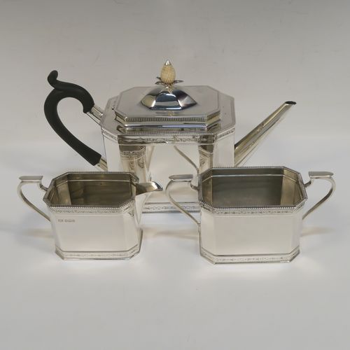 A heavy Sterling Silver three-piece tea set, in a neoclassical style, having plain octagonal bodies with straight sides, applied bead-edged borders above and below bands of bright-cut engraving, with flat-topped scroll side-handles, the teapot with a black wooden scroll handle and a domed lid with bone pineapple finial, and all sitting on flat bases. This beautiful silver three-piece tea set was made by Mappin and Webb of  Sheffield in 1926. The dimensions of this fine hand-made silver tea set are length of teapot 26 cms (10.75 inches), height 13.5 cms (5.3 inches), and the total weight is approx. 1,100g (35.5 troy ounces).   