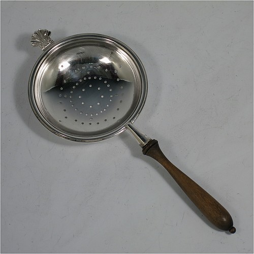 A very handsome, large, and heavy Sterling Silver tea strainer and bowl, having a plain wood-turned handle, a round hand-pierced bowl with an applied reeded border and a cast shell side holder, and sitting on a plain round dregs bowl with three cast hoof feet and shell shoulders. Made by Robert Comyns of London in 1964. The dimensions of this fine hand-made silver tea strainer & bowl are length 19 cms (7.5 inches), diameter of bowl 8 cms (3 inches), with a total weight of approx. 155g (5 troy ounces).    