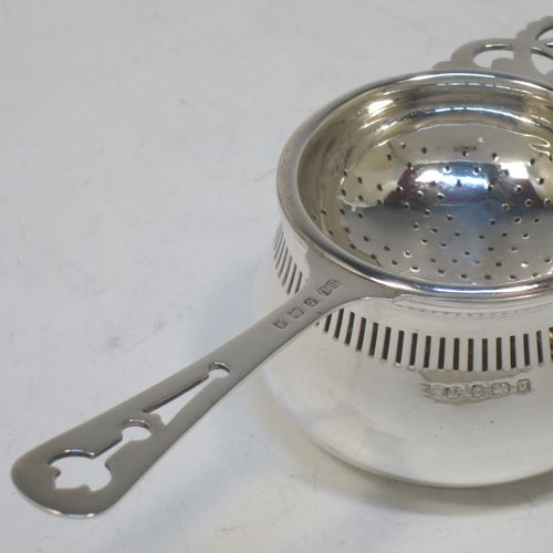 A pretty Sterling Silver tea strainer and bowl, having a hand-pierced handle, a round hand-pierced bowl with hand-cut side holder, and sitting on a plain round dregs stand with a band of piercing and bellied sides. Made by William Suckling Ltd., of Birmingham in 1933. The dimensions of this fine hand-made silver tea strainer & stand are length 14.5 cms (5.75 inches), diameter of stand 6 cms (2.3 inches), with a total weight of approx. 75g (2.4 troy ounces).  