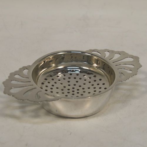 A handsome Sterling Silver tea strainer and dregs bowl in a Georgian lemon strainer style, having a round hand-pierced bowl, with two hand-pierced side-handles, and sitting on an original plain round dregs stand with a flat base. Made by S. C. of Sheffield in 1976. The dimensions of this fine hand-made silver tea strainer and bowl are height 2.5 cms (1 inch), width across handles 11 cms (4.25 inches), and it weighs a total of approx. 78g (2.5 troy ounces).  