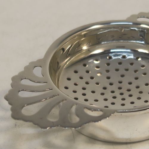 A handsome Sterling Silver tea strainer and dregs bowl in a Georgian lemon strainer style, having a round hand-pierced bowl, with two hand-pierced side-handles, and sitting on an original plain round dregs stand with a flat base. Made by S. C. of Sheffield in 1976. The dimensions of this fine hand-made silver tea strainer and bowl are height 2.5 cms (1 inch), width across handles 11 cms (4.25 inches), and it weighs a total of approx. 78g (2.5 troy ounces).  