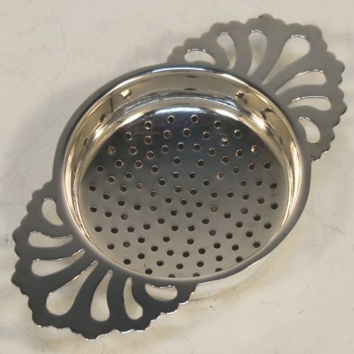 A handsome Sterling Silver tea strainer and dregs bowl in a Georgian lemon strainer style, having a round hand-pierced bowl, with two hand-pierced side-handles, and sitting on an original plain round dregs stand with a flat base. Made by S. C. of Sheffield in 1976. The dimensions of this fine hand-made silver tea strainer and bowl are height 2.5 cms (1 inch), width across handles 11 cms (4.25 inches), and it weighs a total of approx. 78g (2.5 troy ounces).  