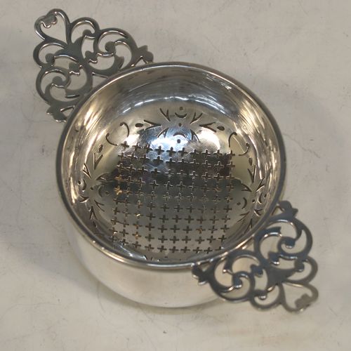 A handsome Sterling Silver tea strainer and dregs bowl in a Georgian lemon strainer style, having a round hand-pierced bowl, with two hand-pierced side-handles, and sitting on an original plain round dregs stand with a flat base. Made by Mappin and Webb of Birmingham in 1930. The dimensions of this fine hand-made silver tea strainer and bowl are height 4 cms (1.5 inches), width across handles 12 cms (4.75 inches), and it weighs a total of approx. 86g (2.8 troy ounces).  