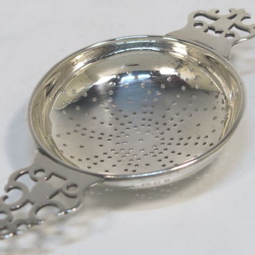 A handsome Sterling Silver tea strainer and dregs bowl in a Georgian lemon strainer style, having a round hand-pierced bowl, with two hand-pierced side-handles, and sitting on an original plain round dregs stand with a reeded border and flat base. This elegant silver tea strainer and bowl was made by Robert Comyns of London in 1940. The dimensions of this fine hand-made silver tea strainer and bowl are height 3.5 cms (1.3 inches), length across handles 12 cms (4.75 inches), and it weighs a total of approx. 80g (2.6 troy ounces).   