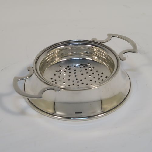 A handsome Antique Sterling Silver tea strainer and dregs bowl in a Georgian lemon strainer style, having a round hand-pierced bowl, with two side-handles, and sitting on an original plain round dregs stand. This elegant antique silver tea strainer and bowl was made by J. B. Carrington of Birmingham in 1921. The dimensions of this fine hand-made silver tea strainer and dregs stand are height 2.5 cms (1 inch), diameter of dregs stand  9.5 cms (3.75 inches), and it weighs a total of approx. 117g (3.8 troy ounces).  