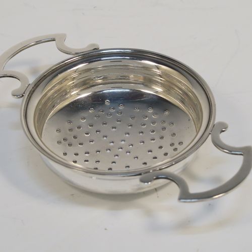 A handsome Antique Sterling Silver tea strainer and dregs bowl in a Georgian lemon strainer style, having a round hand-pierced bowl, with two side-handles, and sitting on an original plain round dregs stand. This elegant antique silver tea strainer and bowl was made by J. B. Carrington of Birmingham in 1921. The dimensions of this fine hand-made silver tea strainer and dregs stand are height 2.5 cms (1 inch), diameter of dregs stand  9.5 cms (3.75 inches), and it weighs a total of approx. 117g (3.8 troy ounces).  