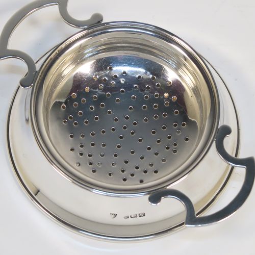 A handsome Antique Sterling Silver tea strainer and dregs bowl in a Georgian lemon strainer style, having a round hand-pierced bowl, with two side-handles, and sitting on an original plain round dregs stand. This elegant antique silver tea strainer and bowl was made by J. B. Carrington of Birmingham in 1921. The dimensions of this fine hand-made silver tea strainer and dregs stand are height 2.5 cms (1 inch), diameter of dregs stand  9.5 cms (3.75 inches), and it weighs a total of approx. 117g (3.8 troy ounces).  