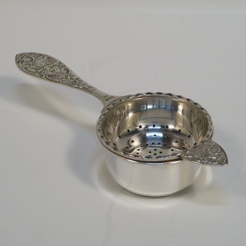 A very pretty Sterling Silver tea strainer and bowl, having a round hand-pierced strainer with an applied wavy-edged border, with a cast side-handle having floral and scroll decoration, and sitting on its original plain round bowl with straight sides and flat base. This beautiful silver tea strainer and bowl was made by John Rose of Birmingham in 1962. The dimensions of this fine hand-made silver tea strainer and bowl are length 15.5 cms (6 inches), diameter of bowl 6 cms (2.3 inches), and with a total weight of approx. 83g (2.7 troy ounces).   