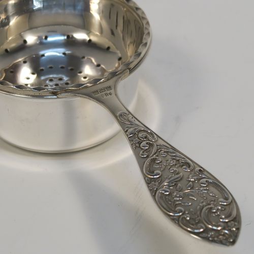 A very pretty Sterling Silver tea strainer and bowl, having a round hand-pierced strainer with an applied wavy-edged border, with a cast side-handle having floral and scroll decoration, and sitting on its original plain round bowl with straight sides and flat base. This beautiful silver tea strainer and bowl was made by John Rose of Birmingham in 1962. The dimensions of this fine hand-made silver tea strainer and bowl are length 15.5 cms (6 inches), diameter of bowl 6 cms (2.3 inches), and with a total weight of approx. 83g (2.7 troy ounces).   