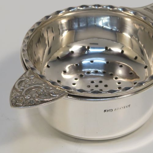 A very pretty Sterling Silver tea strainer and bowl, having a round hand-pierced strainer with an applied wavy-edged border, with a cast side-handle having floral and scroll decoration, and sitting on its original plain round bowl with straight sides and flat base. This beautiful silver tea strainer and bowl was made by John Rose of Birmingham in 1962. The dimensions of this fine hand-made silver tea strainer and bowl are length 15.5 cms (6 inches), diameter of bowl 6 cms (2.3 inches), and with a total weight of approx. 83g (2.7 troy ounces).   