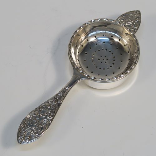 A very pretty Sterling Silver tea strainer and bowl, having a round hand-pierced strainer with an applied wavy-edged border, with a cast side-handle having floral and scroll decoration, and sitting on its original plain round bowl with straight sides and flat base. This beautiful silver tea strainer and bowl was made by John Rose of Birmingham in 1962. The dimensions of this fine hand-made silver tea strainer and bowl are length 15.5 cms (6 inches), diameter of bowl 6 cms (2.3 inches), and with a total weight of approx. 83g (2.7 troy ounces).   