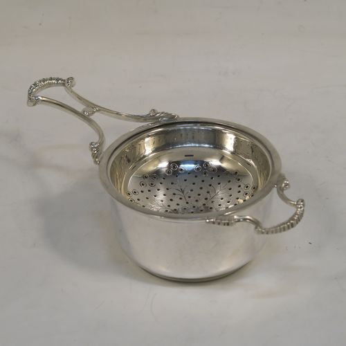 A very pretty Sterling Silver tea strainer and bowl, having a cast scroll side-handle, a round hand-pierced and engraved bowl, and sitting on a plain round dregs bowl. This elegant silver tea strainer and bowl made by Suckling Ltd. of Birmingham in 1958. The dimensions of this fine hand-made silver tea strainer & bowl are length 14 cms (5.5 inches), diameter of bowl 7 cms (2.75 inches), with a total weight of approx. 87g (2.8 troy ounces).   