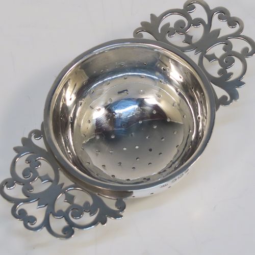 A very stylish Antique Sterling Silver tea strainer and stand, having a round hand-pierced bowl with two florally pierced side-handles, all sitting on an original plain round dregs stand with a wire-work galleried holder on a base with three ball feet. This elegant antique silver tea strainer and stand was made by George Howson of Sheffield in 1920. The dimensions of this fine hand-made antique silver tea strainer and stand are height 4 cms (1.5 inches), length over handles 10 cms (4 inches), and it weighs a total of approx. 80g (2.6 troy ounces).  