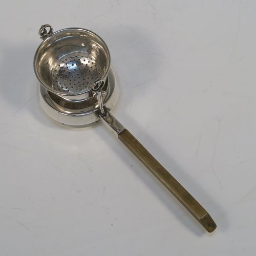 A very unusual Antique Edwardian Sterling Silver gimble-mounted tea strainer on a teapot style stand, having a round hand-pierced bowl mounted on two side stands, all sitting on an original plain round dregs stand in the shape of a teapot, together with an original wooden insulated side-handle. This rare antique silver tea strainer and stand was made by Fredericks Ltd., of London in 1907. The dimensions of this fine hand-made antique silver tea strainer and stand are height 5.5 cms (2.25 inches), length including handle 17 cms (6.75 inches), and it weighs a total of approx. 50g (1.6 troy ounces).   