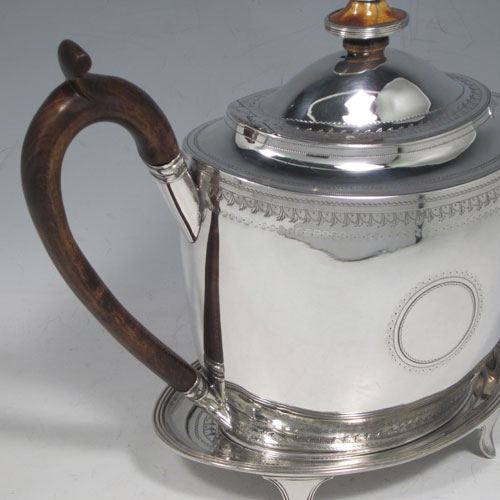 Antique Georgian sterling silver teapot on stand, having a hand-engraved oval body, with bands of floral decoration, a hinged domed lid with silver bound ivory finial, a wooden scroll handle, and sitting on its original stand with four flanged feet and reeded border. Made by Thomas Robins of London in 1800. The dimensions of this fine hand-made silver teapot on stand are length 28 cms (11 inches), height (on stand) 19 cms (7.5 inches), and it weighs approx. 543g (17.5 troy ounces).